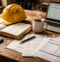 Construction contractor reviewing CIS documents and accounting records at a project site office desk with hardhat and invoices