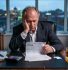 A UK company director at a desk at dawn, staring at a CT600 form with a large figure circled in red pen. Calculator beside the papers, cold tea to the side. Quiet dread. Placed at the very top of the article.