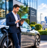 A UK SME owner standing next to an electric company car outside a modern office, reviewing tax savings on a tablet.